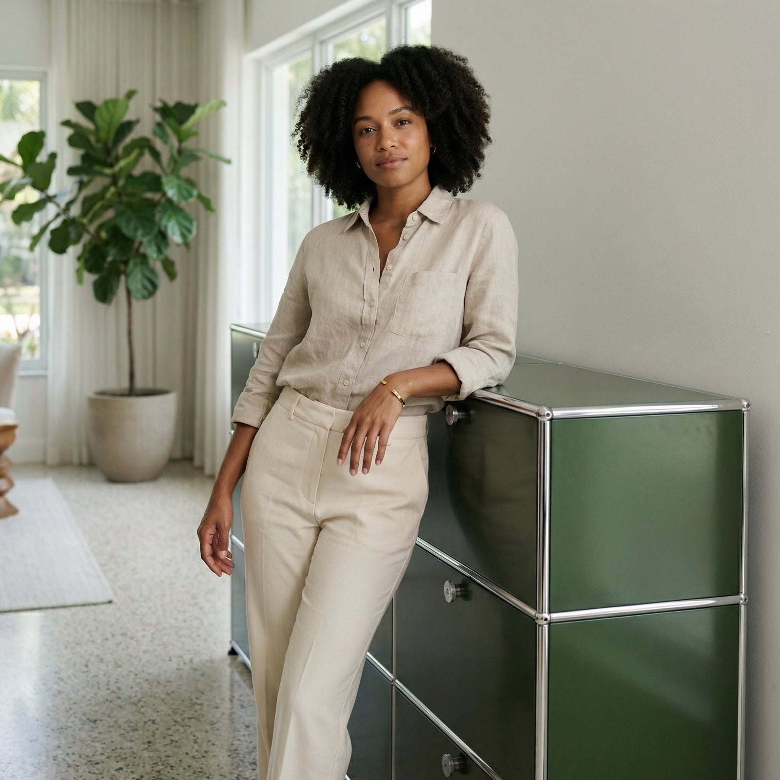 Lifestyle image of a woman leaning on an olive green USM Haller storage unit in a bright modern interior