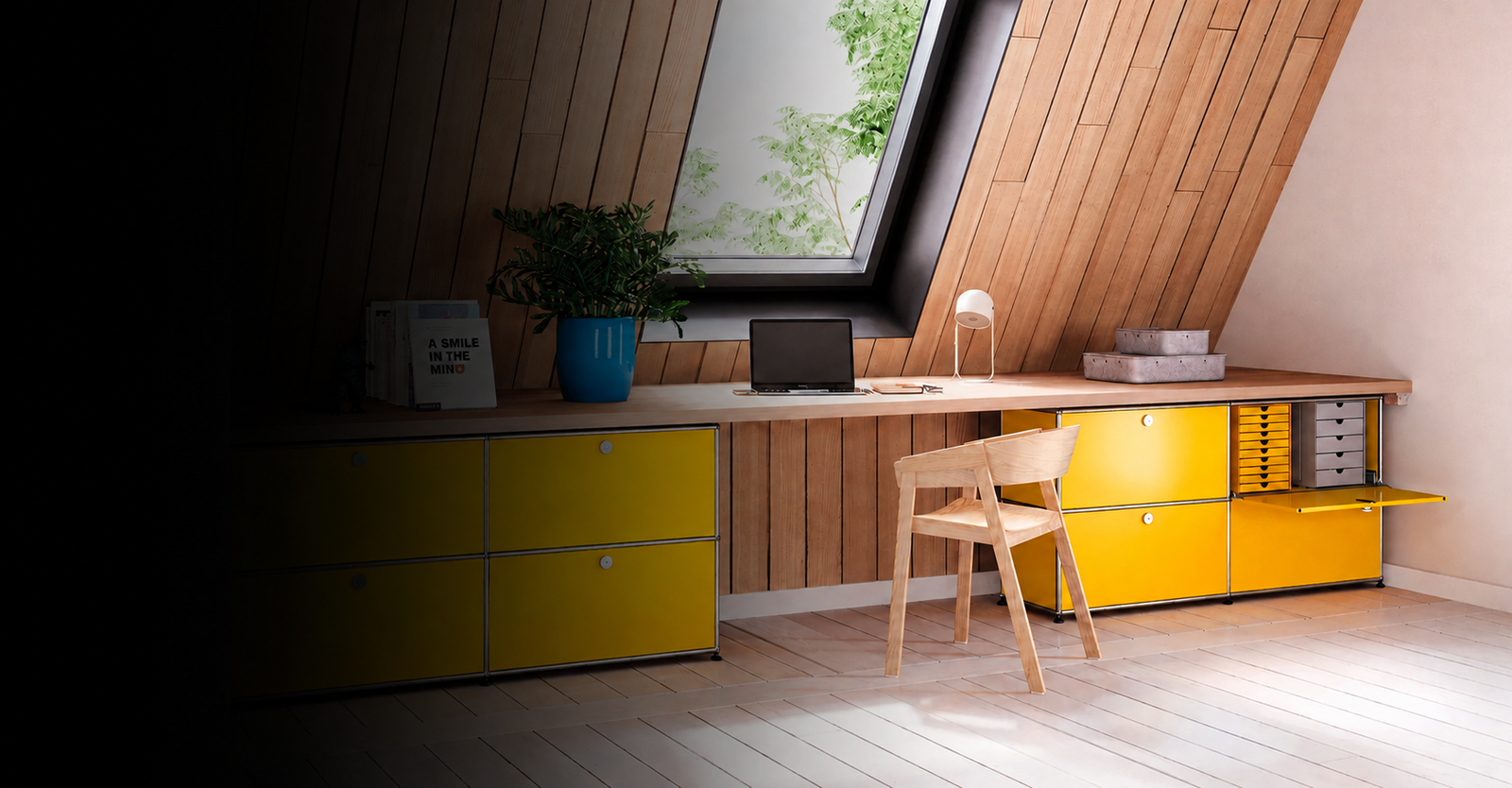 A modern desk setup in an attic room with wood-paneled walls and a large skylight. The desk features bright yellow storage cabinets on the left and right, a light wood desk surface, a matching wooden chair, and various desk accessories including a laptop, lamp, and potted plant.