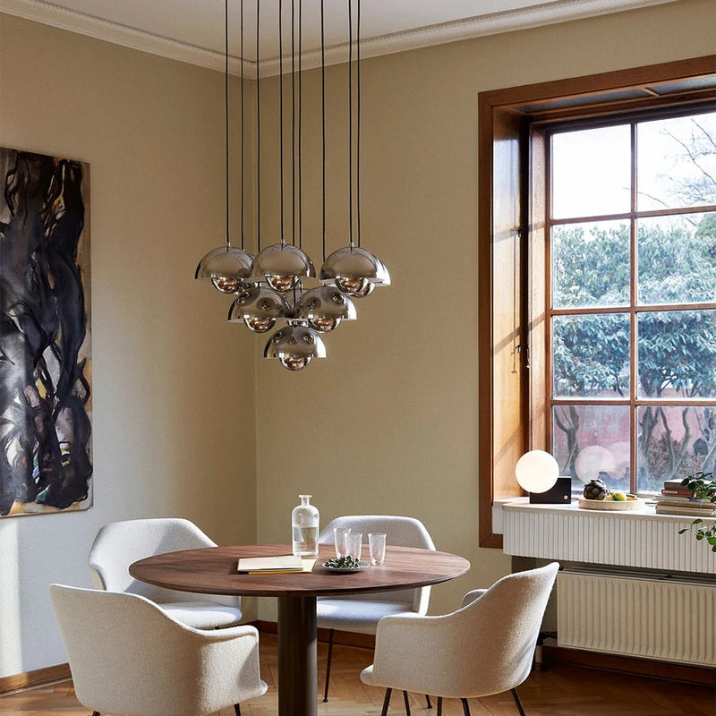 A split-view interior scene showing a dining room with a round wooden table, four white chairs, and a hanging chandelier, alongside a close-up of a gray dome pendant light against a wood panel and gray wall.